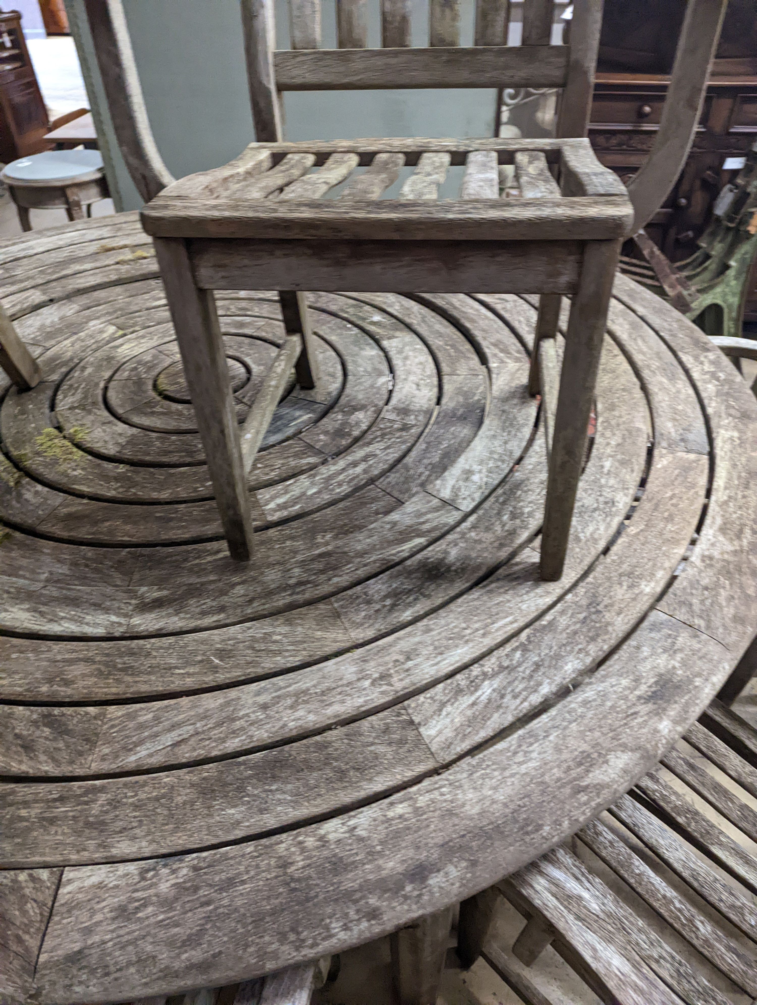 An Alexander Rose weathered teak circular garden table, diameter 190cm, height 74cm and eight elbow chairs